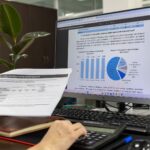En person som granskar tryckta dokument framför en datorskärm.