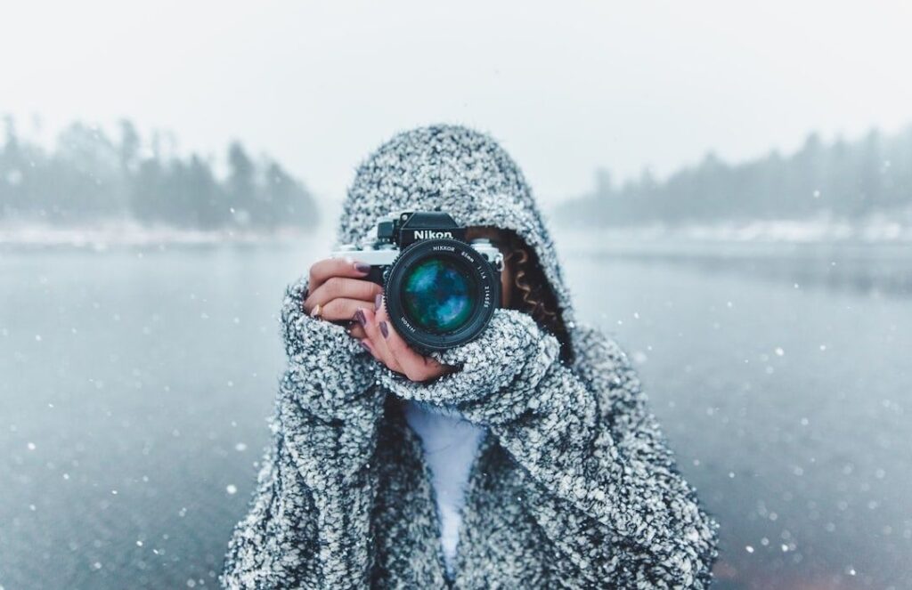 Fotograf i snöfall håller en Nikon-kamera vid en isig sjö