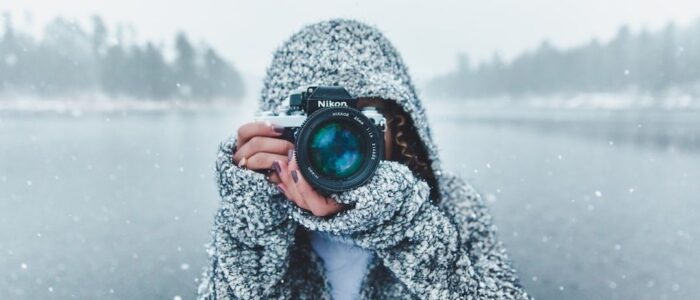 Fotograf i snöfall håller en Nikon-kamera vid en isig sjö