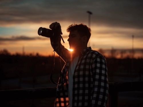 Fotograf i motljus vid solnedgång med kamera framför ansiktet